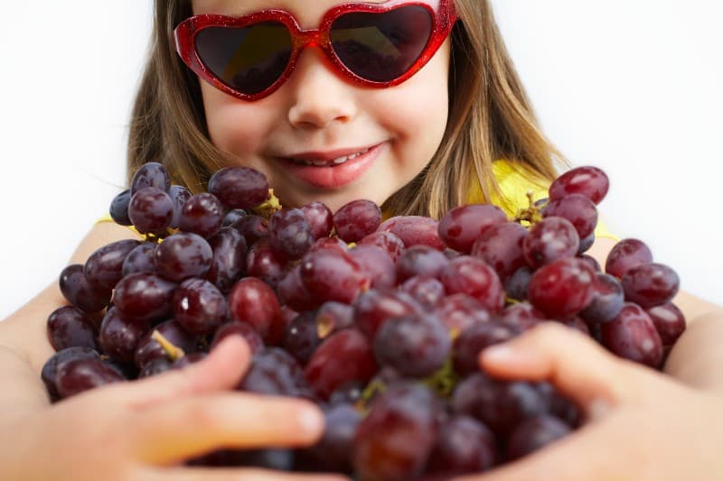 A girl with heart shaped glasses holds a very large bunch of grapes. What is she going to do with all of those grapes?