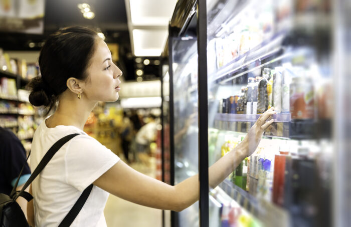 A teen girl looks into a cold case with beverages at a grocery store