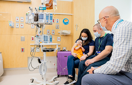 A mother holds her infant daughter while sitting next to her husband and a make doctor in a hospital room