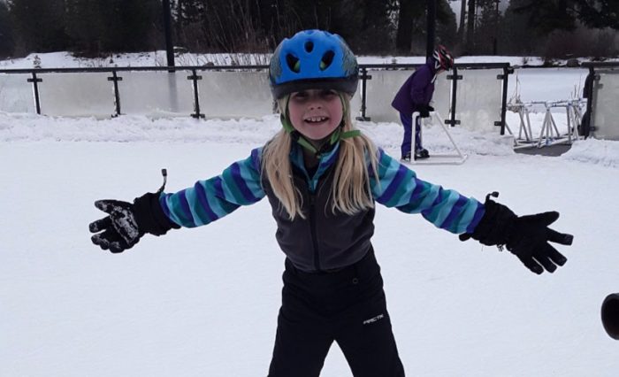 A girl in snow gear and a ski helmet spreading her arms wide as she stands in the snow