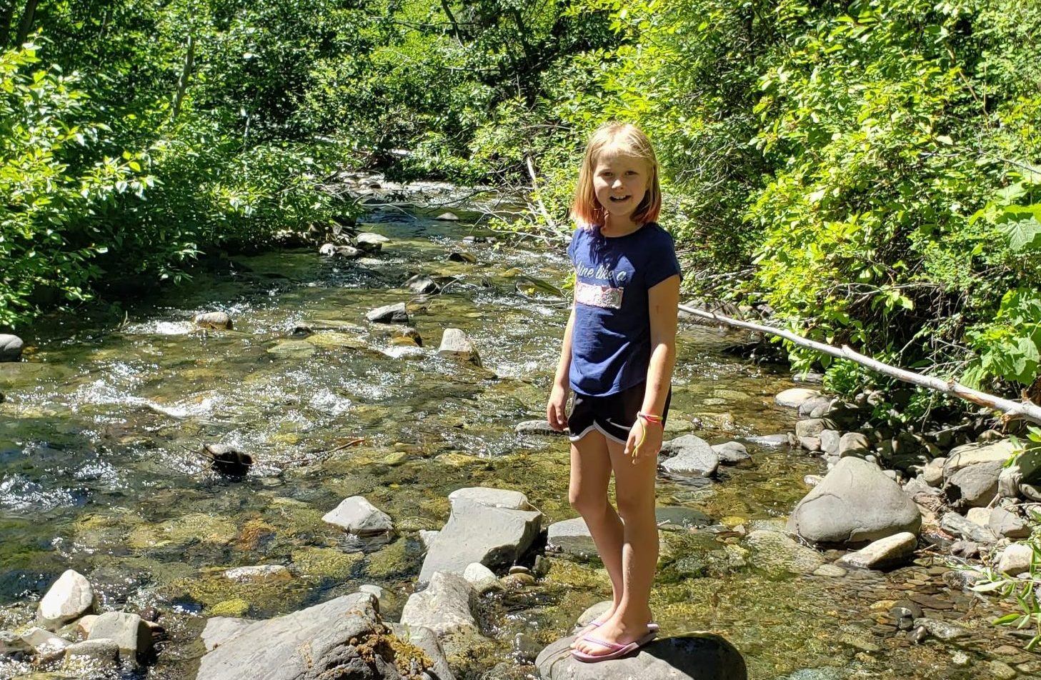 A school aged girl smiles and poses on a streambed.