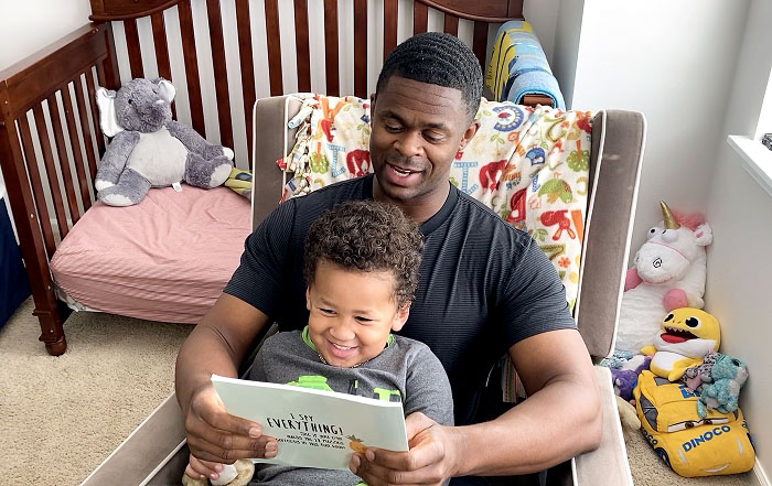 A son happily sits on his dad's lap in while he reads him a book