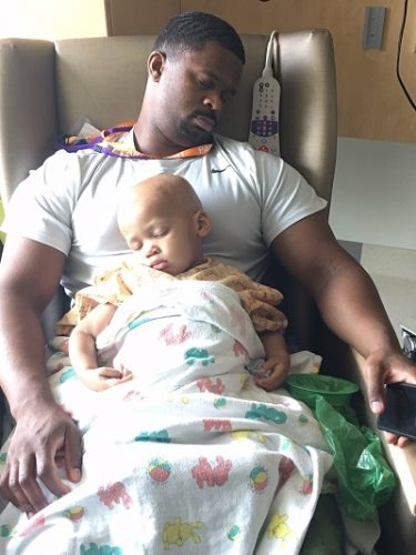 A son sleeps on his dad's lap while in the hospital