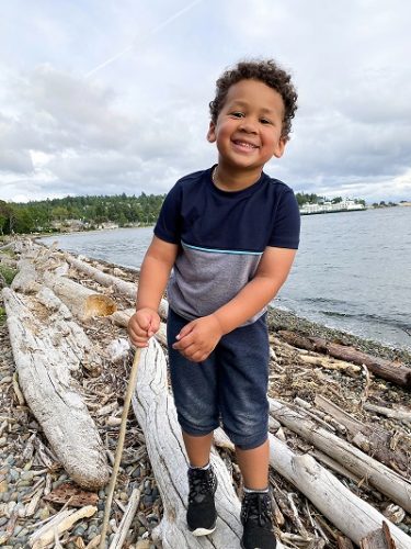 A little boy walks across driftwood on a Pacific Northwest beach