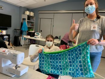 Two young women show off a blanket they created