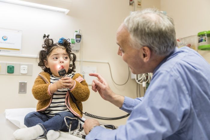 A little girl holds a light from her doctor's stethoscope in her mouth while her doctor watched