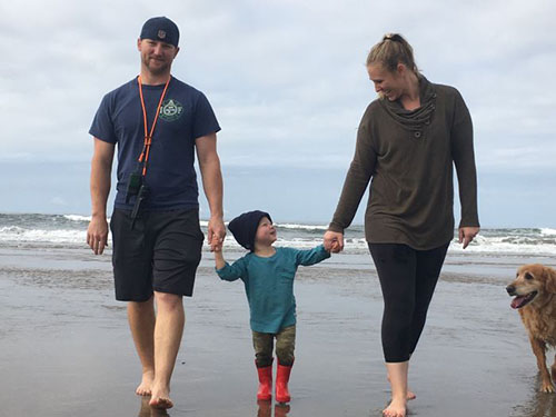 A boy holds hand with his mother and father on a beach