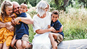 A man, woman, daughter and two sons smile happily as they sit together on a log in a field