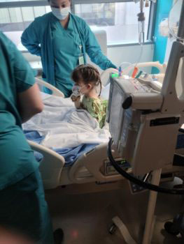 A toddler in a hospital bed, surrounded by medical professionals