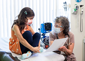 A provider shows a girl something on a paper while she sits on an exam table