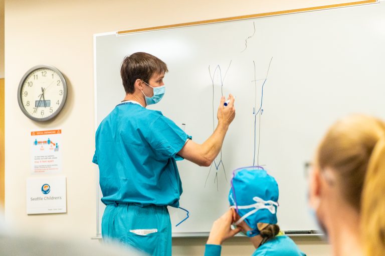 A doctor writes on a whiteboard while others look on