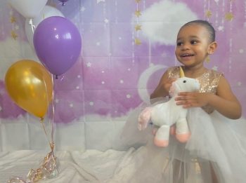 A girl in a dress holding a unicorn stuffie