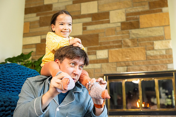 A little girl smiles while sitting on a man shoulders, with her hands clasped on his head and his hands holding her ankles for balance