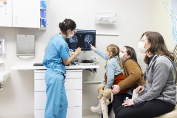 A little girl points at a computer screen with an image of her brain