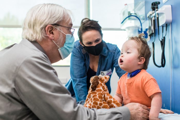 A doctor examines a young boy while his mom smiles at him