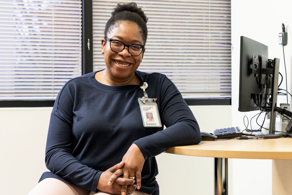 Dr. Yolanda Evan smiles at the camera while sitting at a desk with a computer