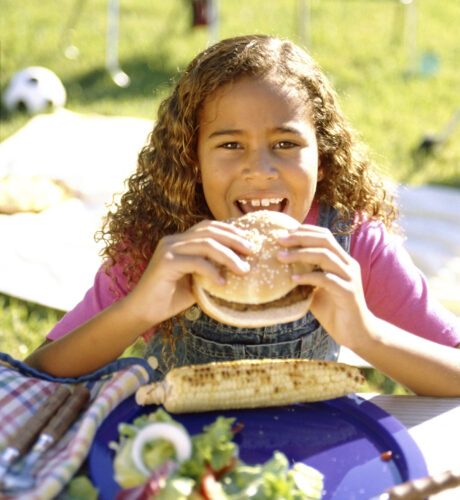 A girl eats a grilled burger at a picnic