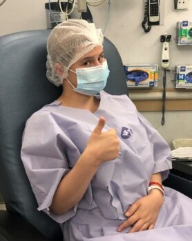 A teen girl gives a thumbs up in a hospital