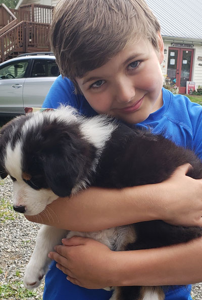 A young boy cuddles his black and white puppy while looking at the camera