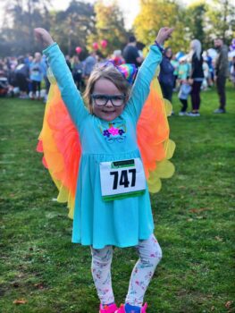 A little girl in a blue dress with butterfly wings off the sleeves, smiles so big for the camera