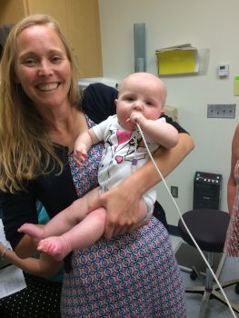 A female doctor smiles as she holds a baby girl in a hospital room