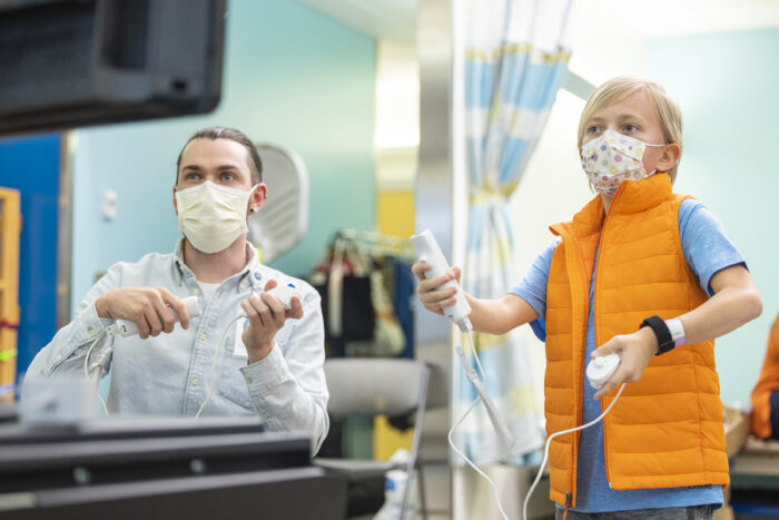 A patient and his child life therapist hold video game controllers as they play a game together