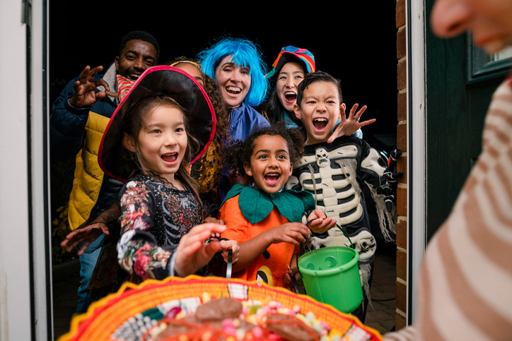 A group of excited trick or treaters in costumes from the perspective of the inside of an open front door.