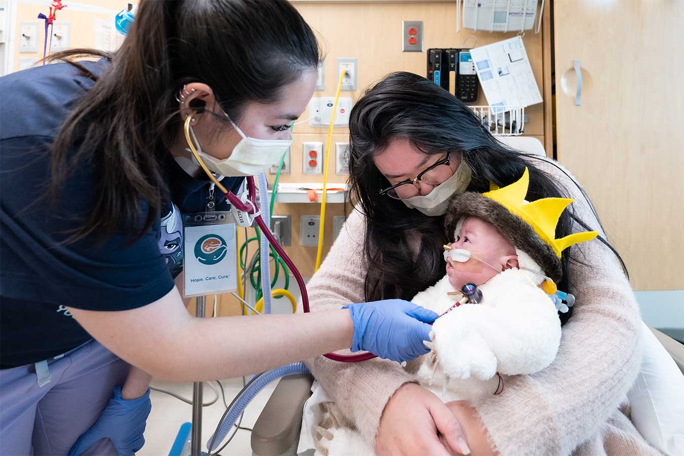 A nurse with a stethoscope tends to a baby being held by its mother 