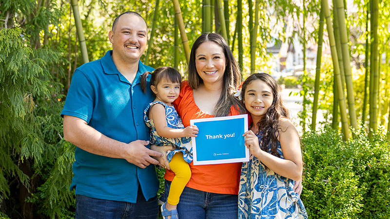 A family standing outside holds a sign that reads "Thank you!"