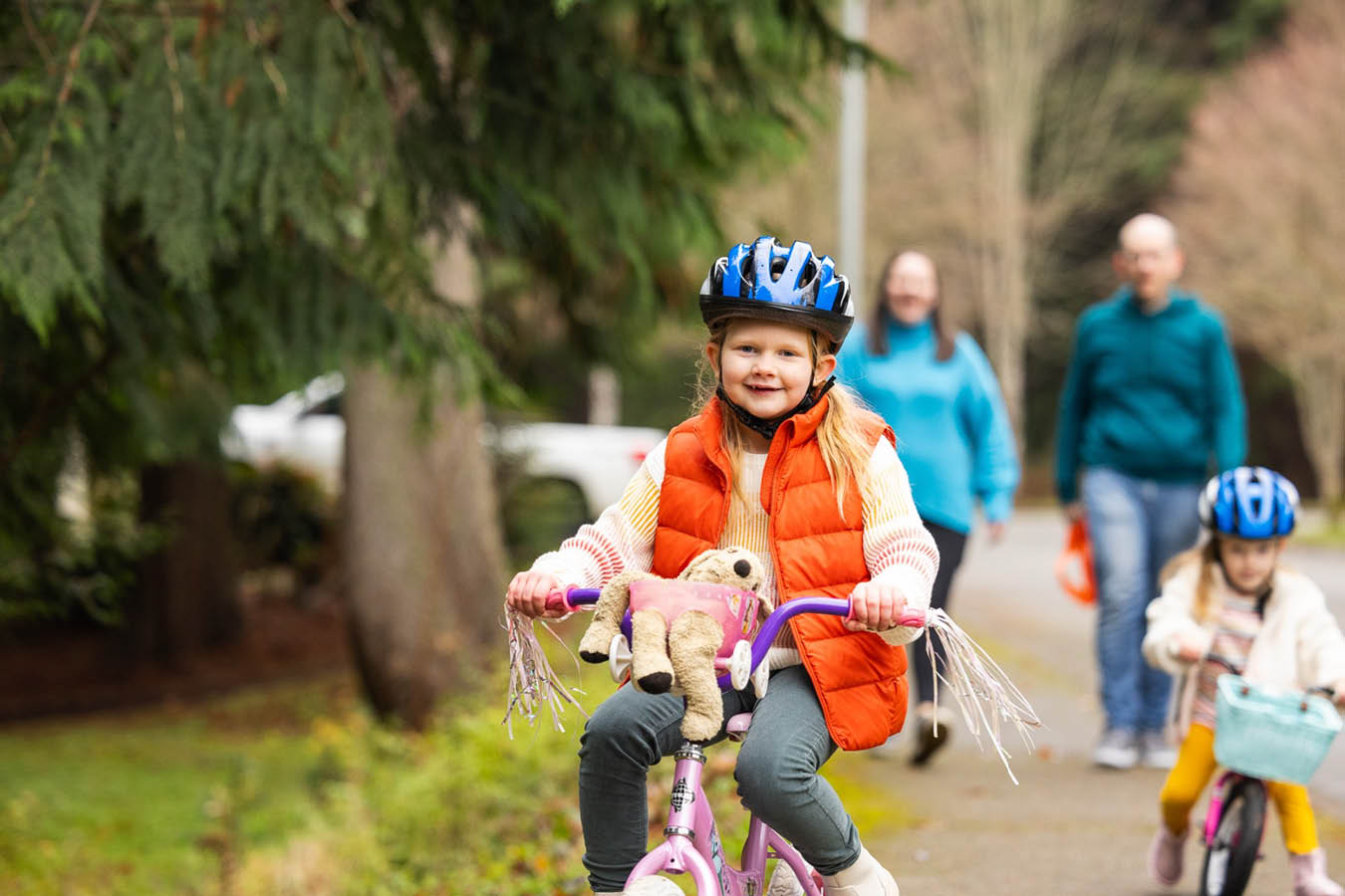 A girl in a bike helmet rides a bike in front of her family