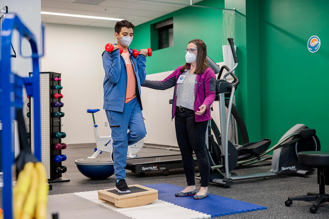 A boy lifts dumbbells with a sports physical therapist