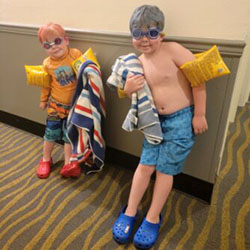 Two boys wearing bathing suits and swim goggles.