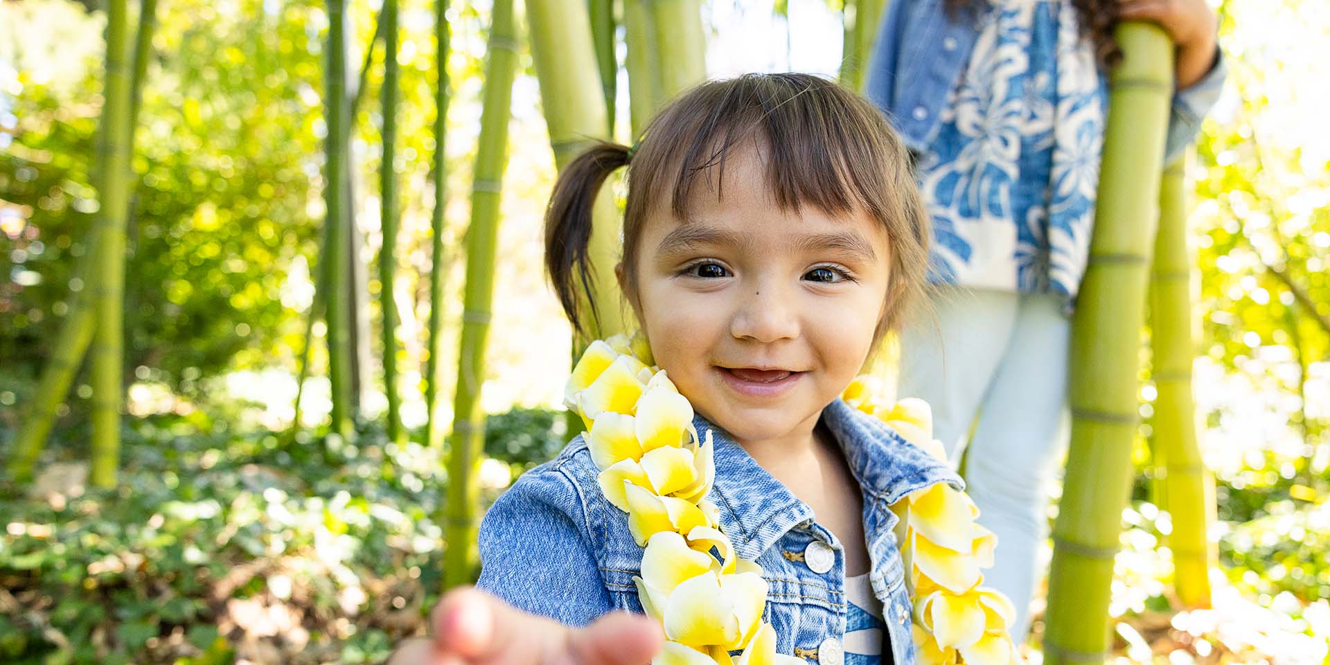 A girl wearing a lei poses for the camera with bamboo growing behind her