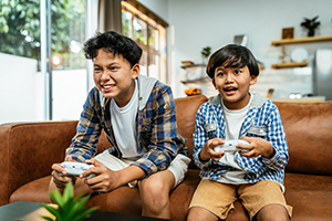 Two brothers sitting beside each other on a tan leather couch while holding game controllers with very animated expressions on their faces as they stare straight ahead