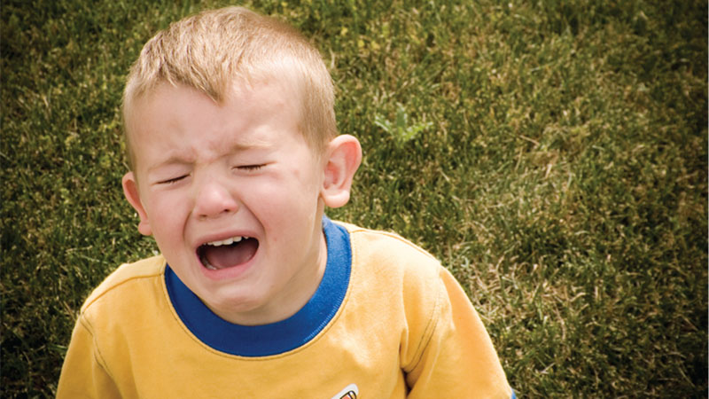 A boy having a tantrum while sitting on grass