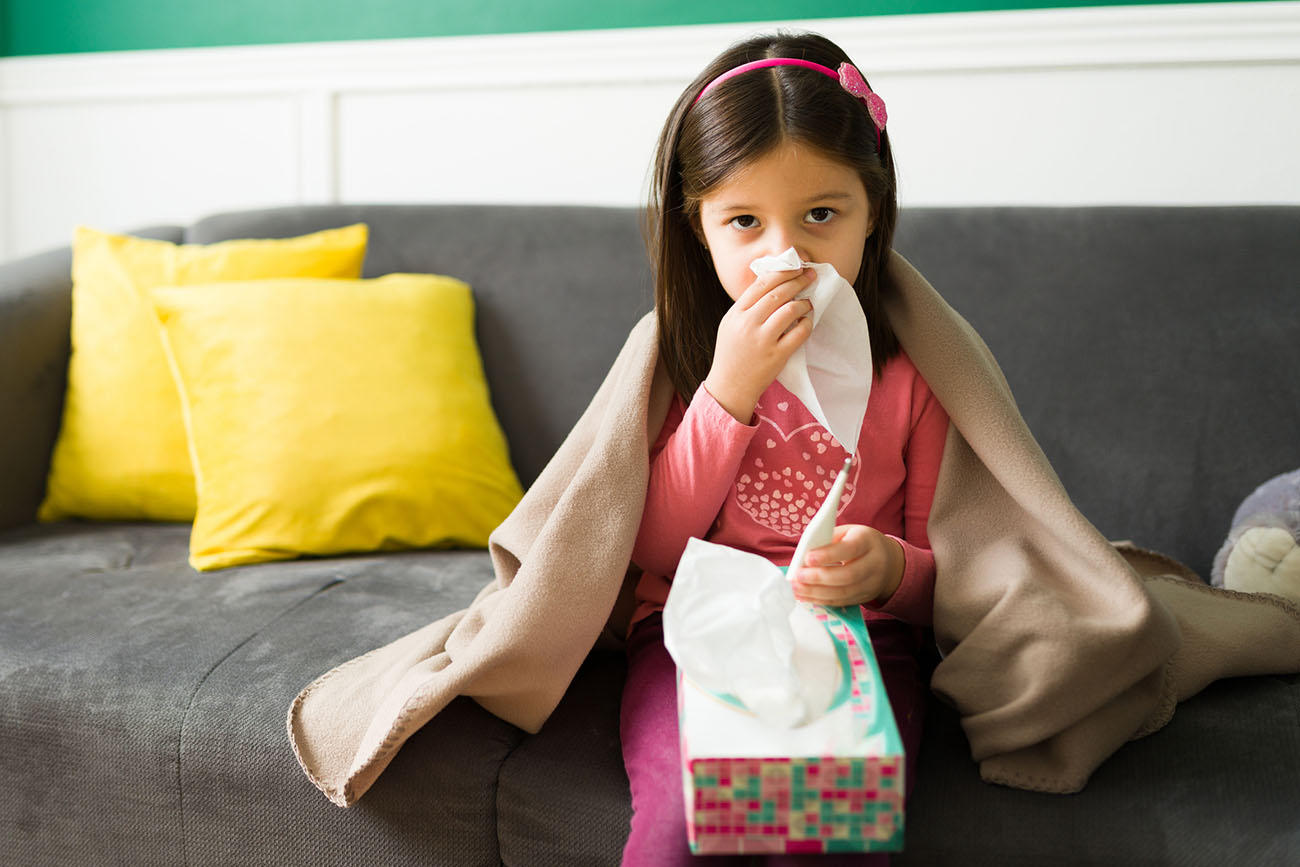 A girl blows her nose into a tissue while sitting on a couch