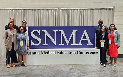 People stand next to a sign that reads "SNMA: Annual Medical Education Conference"