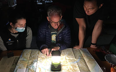 Three people huddle around a camp light, looking at a map