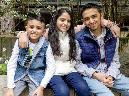 Three siblings sitting in front of a garden